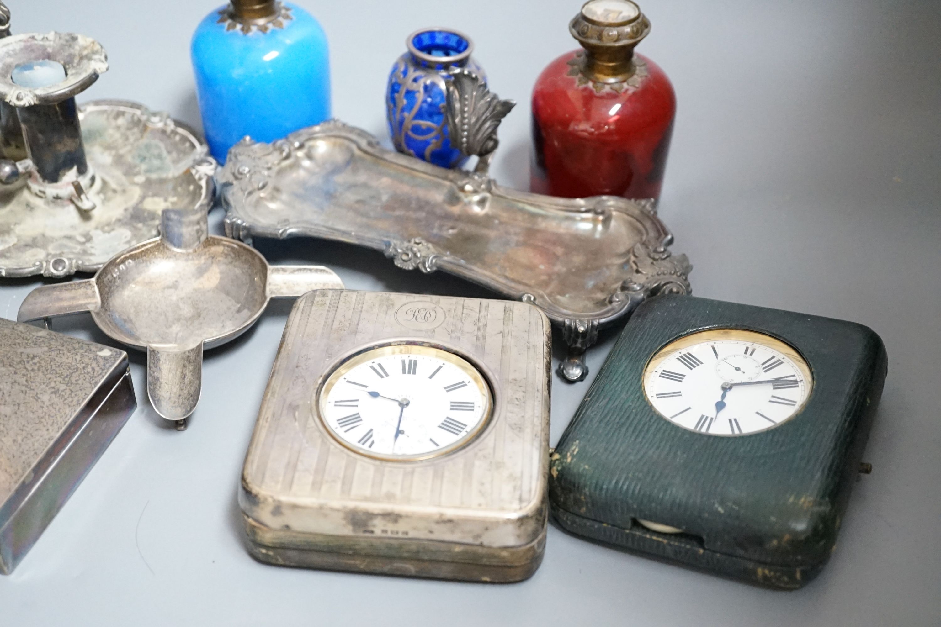 An Edwardian silver mounted travelling pocket watch case with 8-day pocket watch, one other travelling pocket watch in case, a silver mounted cigarette box, a silver ashtray, a plated snuffers stand and plated chambersti